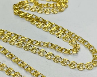 May include: Close-up of multiple gold-colored chain necklaces. The chains have a delicate, intricate design with a repeating pattern of linked loops. The chains are displayed against a light background.