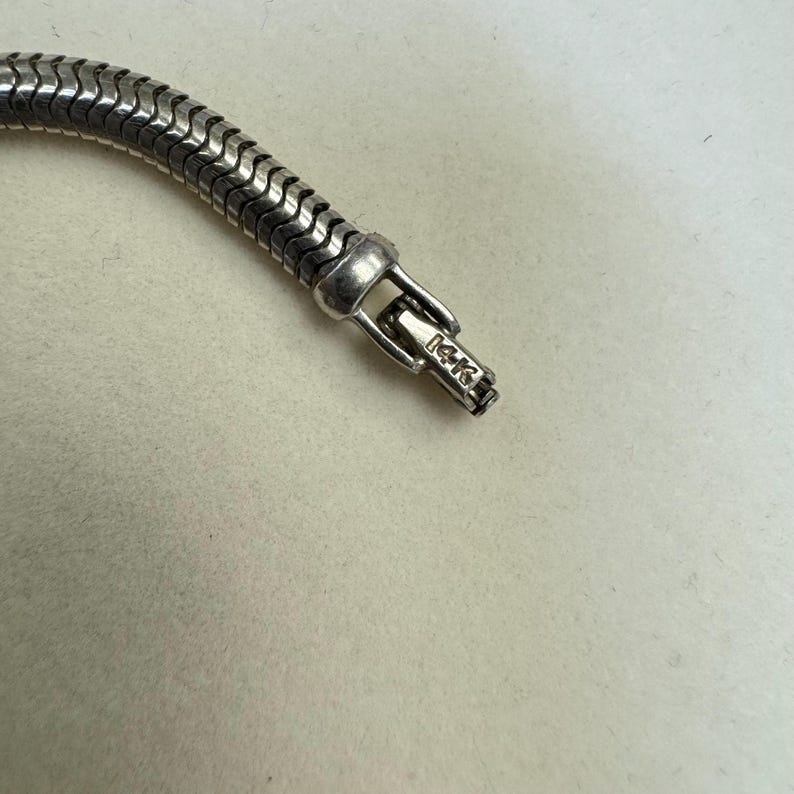 K&ouml;nnte beinhalten: Nahaufnahme einer silbernen Kettenkette mit einem Verschluss, auf dem "14k" steht.