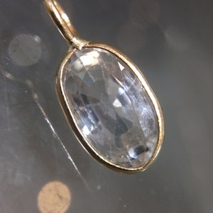 May include: A gold pendant with a clear oval-shaped gemstone. The pendant is on a white background.