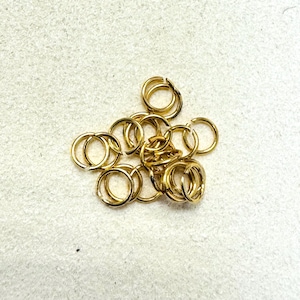 May include: A pile of small, gold-colored jump rings. These open rings are used in jewelry making and other crafts. The rings are round and have a split, allowing them to be opened and closed to connect other components.