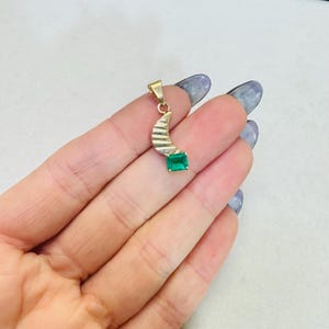 K&ouml;nnte beinhalten: Goldener Anh&auml;nger mit einem Halbmond-Design und einem rechteckigen, smaragdgeschliffenen gr&uuml;nen Edelstein. Der Anh&auml;nger hat ein strukturiertes, gestreiftes Muster auf dem gebogenen Teil.