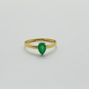 May include: A gold ring featuring a pear-shaped, vibrant green gemstone. The ring's band is a simple, polished gold, and the gemstone is the focal point, set in a classic prong setting. The ring is displayed against a plain white background.