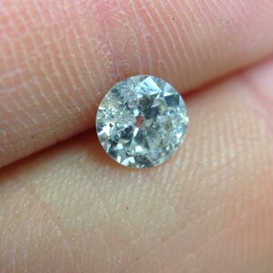 May include: A clear, round, faceted gemstone with a slight blue hue. The gemstone is set in a silver bezel.