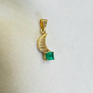 K&ouml;nnte beinhalten: Goldener Anh&auml;nger mit einem Halbmond-Design und einem quadratischen, smaragdgr&uuml;nen Edelstein. Der Anh&auml;nger hat eine Schlaufe f&uuml;r eine Kette. Der Edelstein ist etwa 0,6 cm gro&szlig;.