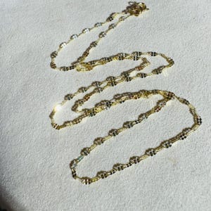 May include: A gold chain necklace with a delicate, interwoven design. The chain is made of multiple strands of gold, creating a layered effect.