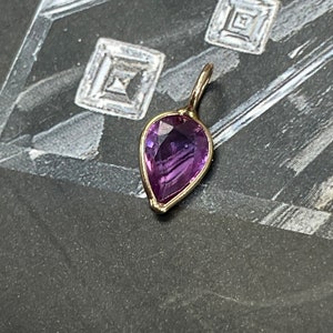 May include: A purple gemstone pendant with a pear-shaped cut, set in gold.
