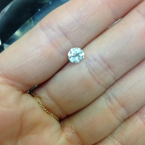 May include: A clear round diamond gemstone held in a hand.