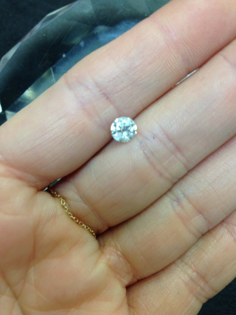 May include: A clear round diamond gemstone held in a hand.