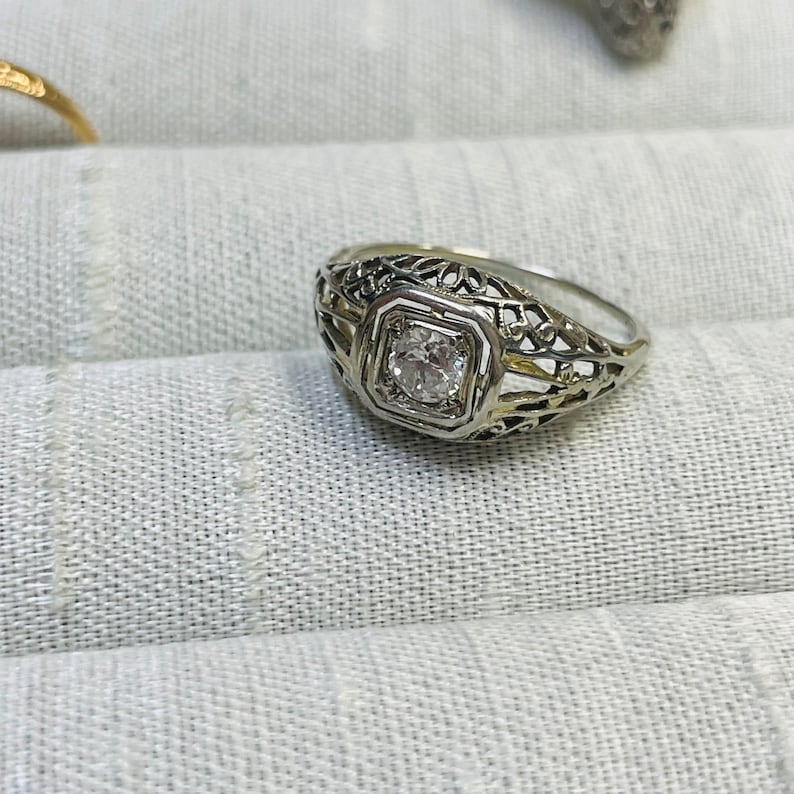 May include: A silver filigree ring with a single round diamond in the center.