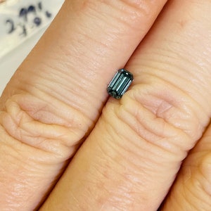 May include: A dark blue emerald cut gemstone with a rectangular shape.