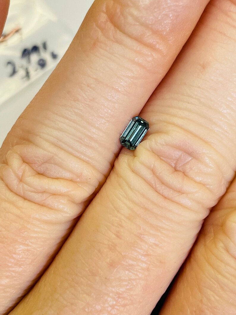 May include: A dark blue emerald cut gemstone with a rectangular shape.
