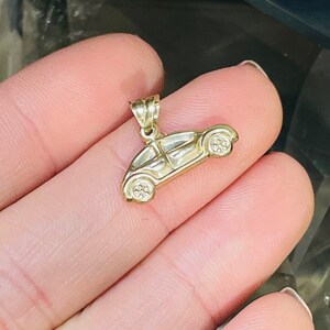 May include: A gold-colored car charm pendant. The charm is in the shape of a classic car with a rounded body and detailed wheels.