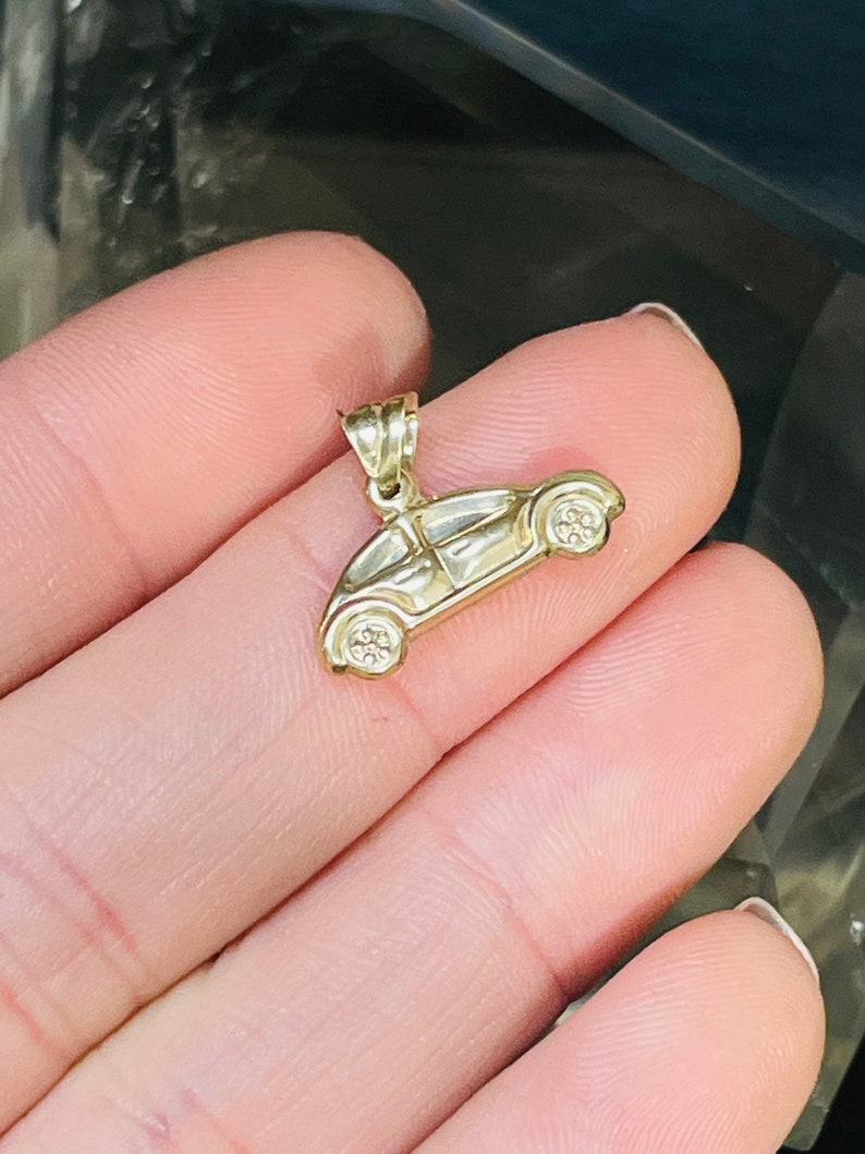 May include: A gold-colored car charm pendant. The charm is in the shape of a classic car with a rounded body and detailed wheels.