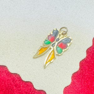 Puede incluir: Encanto de mariposa de tono dorado con acentos de esmalte rojo, verde, negro y amarillo.