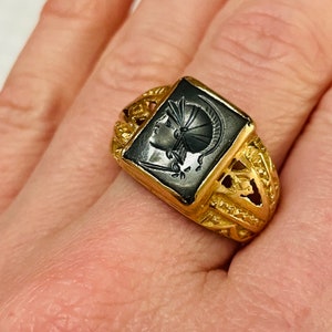 May include: A gold ring with a black onyx stone featuring a carved image of a woman's head. The ring has a detailed, ornate design.
