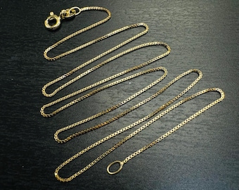 May include: A gold chain necklace with a box clasp and a lobster claw clasp. The chain is made of small, linked squares.