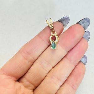 May include: A gold pendant with a teardrop-shaped, green gemstone. The pendant has an ornate design with a loop at the top for a chain. The gemstone is a vibrant green color, and the gold has a polished finish.