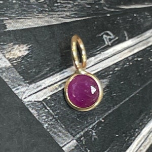 May include: A gold pendant with a small oval-shaped ruby gemstone.