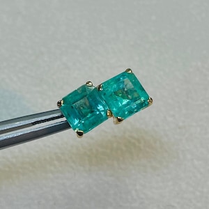 May include: A pair of emerald green square-shaped earrings with gold settings.