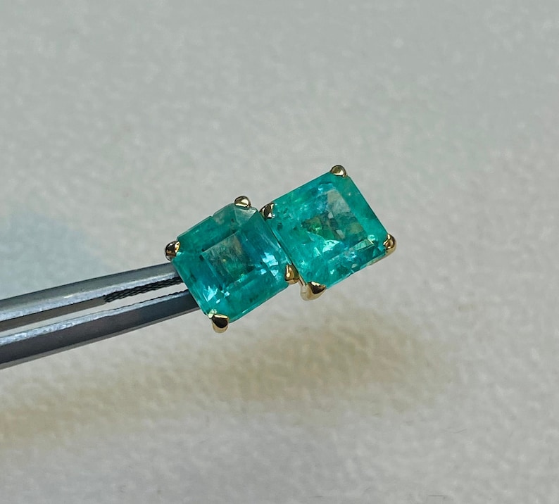 May include: A pair of emerald green square-shaped earrings with gold settings.