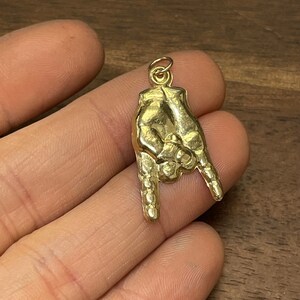 Peut inclure: Un pendentif en or en forme de main faisant le geste 'rock on'. Le pendentif est détaillé avec des doigts texturés et un pouce surélevé.