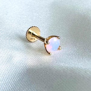 May include: A gold-colored, 14K threaded stud earring with a faceted, light pink opal gemstone. The earring has a flat, textured backing and a prong setting to secure the gemstone.