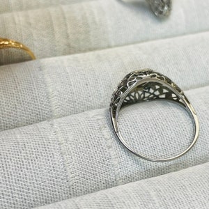 May include: A silver filigree ring with a delicate design. The ring is set with a small, round stone in the center.