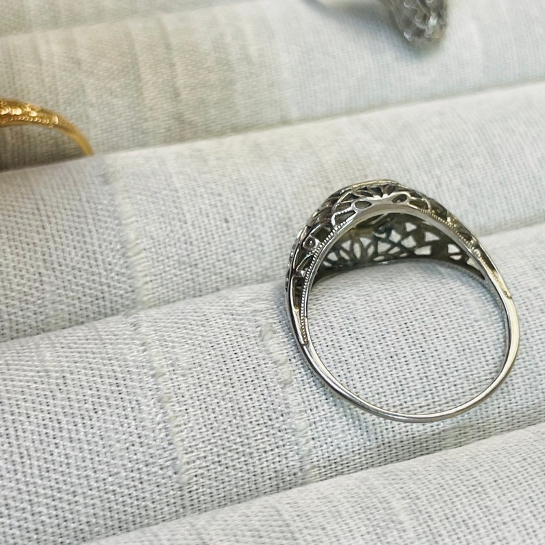 May include: A silver filigree ring with a delicate design. The ring is set with a small, round stone in the center.