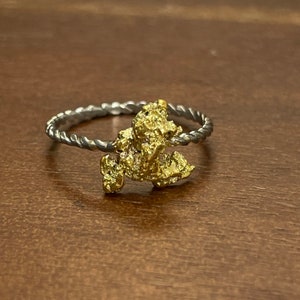 Puede incluir: Un anillo de banda retorcida de plata con una piedra en forma de pepita de oro.