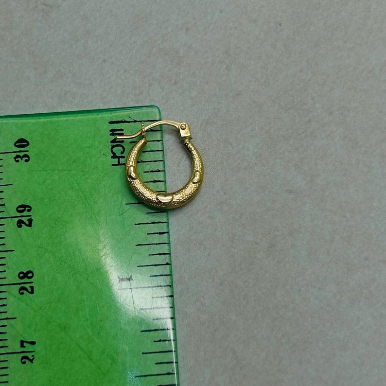 Puede incluir: Pendientes de aro de oro con superficie texturizada. Los pendientes se miden con una regla.