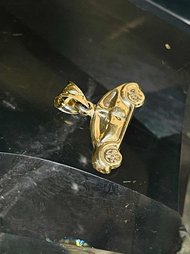 May include: A gold-colored car charm pendant. The charm is detailed and has a realistic design.