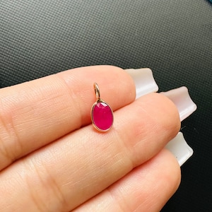 以下が含まれることがあります： 金色の枠にセットされた明るいピンクの宝石が付いた、小さな楕円形のペンダント