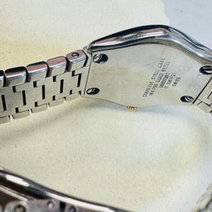 Pode incluir: Close-up de um rel&oacute;gio de a&ccedil;o inoxid&aacute;vel com uma pulseira prateada. A caixa do rel&oacute;gio tem o texto "STAINLESS STEEL CASE 18K 750 GOLD BEZEL 56600397 C 1087F21 SWISS". O rel&oacute;gio est&aacute; sobre uma superf&iacute;cie clara.