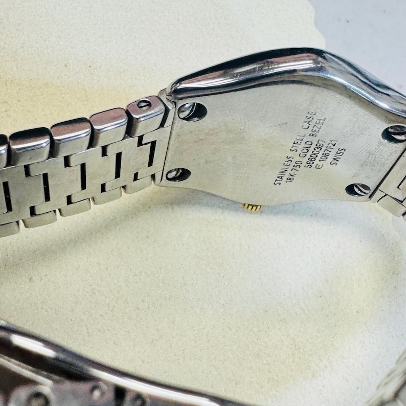 Pode incluir: Close-up de um rel&oacute;gio de a&ccedil;o inoxid&aacute;vel com uma pulseira prateada. A caixa do rel&oacute;gio tem o texto "STAINLESS STEEL CASE 18K 750 GOLD BEZEL 56600397 C 1087F21 SWISS". O rel&oacute;gio est&aacute; sobre uma superf&iacute;cie clara.