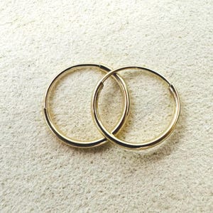 May include: A pair of gold-coloured hoop earrings. The earrings are circular with a smooth, polished finish. The hoops are interlocked, indicating they are a set. The background is a light, textured surface.