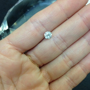 May include: A clear round gemstone with facets, held in a hand.