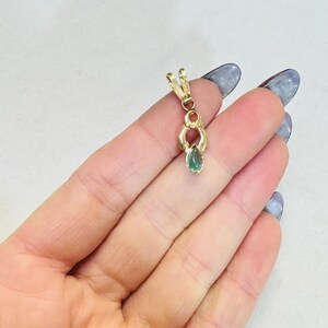 May include: A gold pendant with a teardrop-shaped green gemstone. The pendant has a decorative design with a loop at the top for a chain. The gemstone is a vibrant green color.