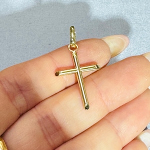 Op de afbeelding: Een gepolijste gouden kruishanger met een eenvoudig, slank ontwerp met afgeronde randen en een kleine ronde ring aan de bovenkant voor bevestiging. Het kruis heeft een glad, reflecterend metalen oppervlak en een strakke, eenvoudige structuur.