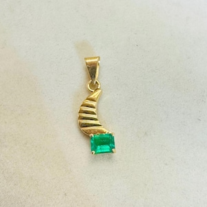 K&ouml;nnte beinhalten: Goldener Anh&auml;nger mit einem Halbmond-Design mit ge&auml;tzten Linien und einem rechteckigen, smaragdgr&uuml;nen Edelstein. Der Anh&auml;nger hat eine kleine Schlaufe f&uuml;r eine Kette.