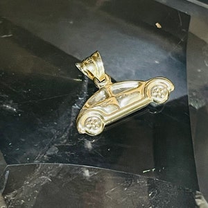 May include: A gold-colored charm in the shape of a classic Volkswagen Beetle car. The charm has a loop at the top for attaching to a necklace or bracelet.