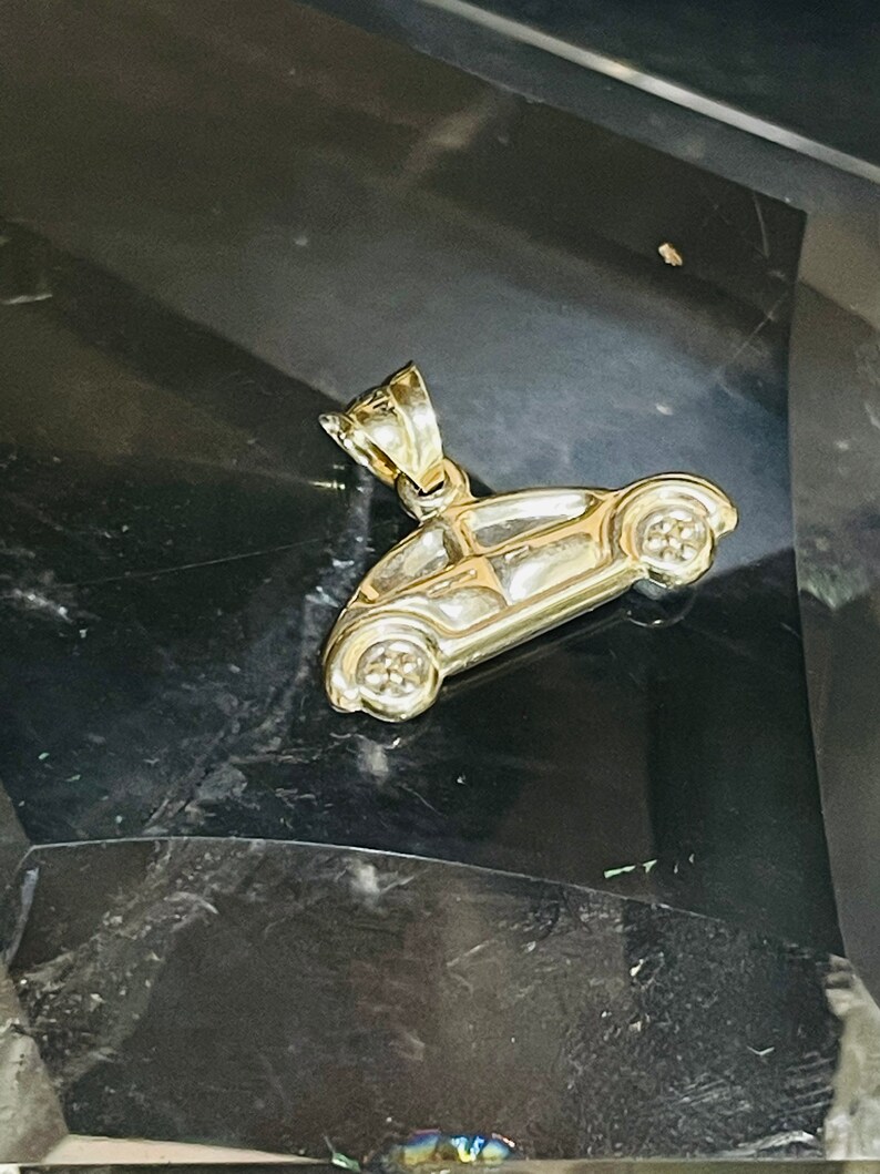 May include: A gold-colored charm in the shape of a classic Volkswagen Beetle car. The charm has a loop at the top for attaching to a necklace or bracelet.