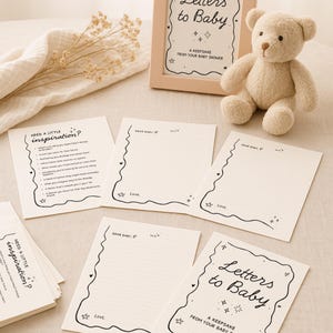 May include: A collection of baby shower keepsakes, including cards with the text "Letters to Baby" and "Need a Little Inspiration?" in black script. A beige teddy bear and a framed sign are also present, creating a soft, neutral color palette.