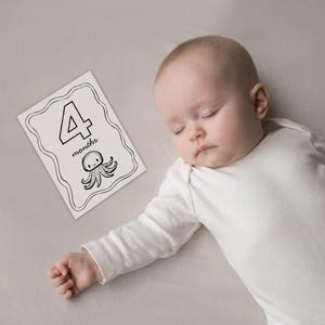 Peut inclure: Un b&eacute;b&eacute; en body blanc est allong&eacute; &agrave; c&ocirc;t&eacute; d'une carte &eacute;tape noir et blanc. La carte affiche le chiffre "4", le mot "mois" et une illustration de poulpe de dessin anim&eacute;.