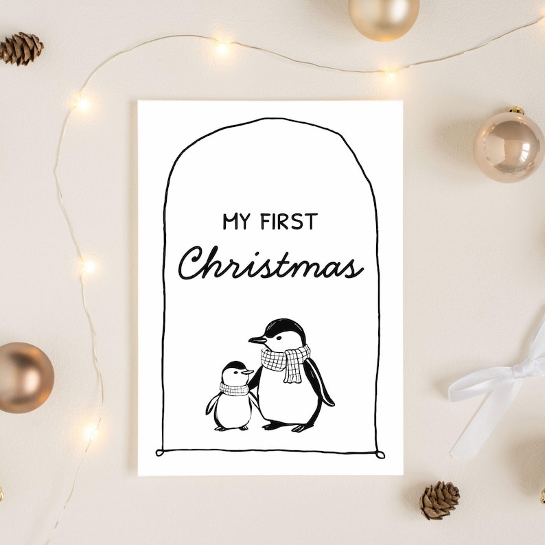 Peut inclure: Carte de v&oelig;ux en noir et blanc avec l'inscription "MY FIRST Christmas". Elle repr&eacute;sente deux pingouins, un adulte et un b&eacute;b&eacute;, portant des &eacute;charpes. La carte est entour&eacute;e de d&eacute;corations de No&euml;l.