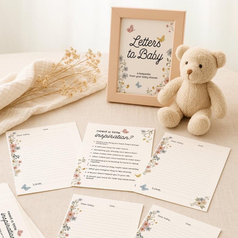 Op de afbeelding: Een aandenken set voor een babyshower met een ingelijste print met de tekst "Letters to Baby", een teddybeer en verschillende gelijnde kaarten met bloemen- en vlinderaccenten. De kaarten bevatten prompts voor het schrijven van brieven.