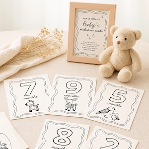 Peut inclure: Cartes &eacute;tapes pour b&eacute;b&eacute; avec illustrations et chiffres en noir et blanc. Un cadre indique "Cartes &eacute;tapes de b&eacute;b&eacute;". Un ours en peluche beige est pos&eacute; &agrave; c&ocirc;t&eacute; des cartes. Les cartes repr&eacute;sentent les mois 2, 5, 7, 8 et 9.