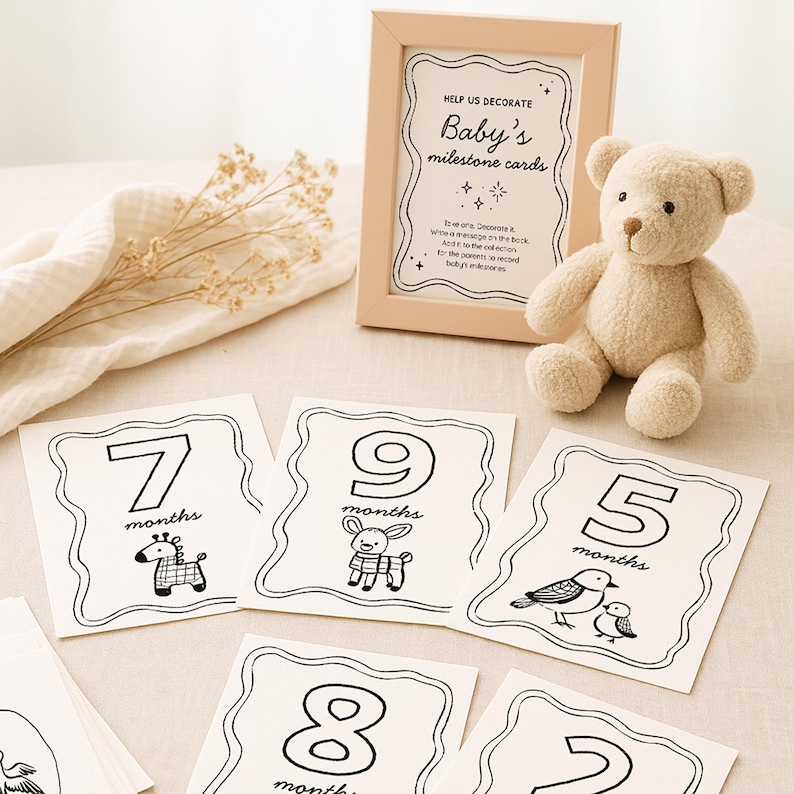 Peut inclure: Cartes &eacute;tapes pour b&eacute;b&eacute; avec illustrations et chiffres en noir et blanc. Un cadre indique "Cartes &eacute;tapes de b&eacute;b&eacute;". Un ours en peluche beige est pos&eacute; &agrave; c&ocirc;t&eacute; des cartes. Les cartes repr&eacute;sentent les mois 2, 5, 7, 8 et 9.