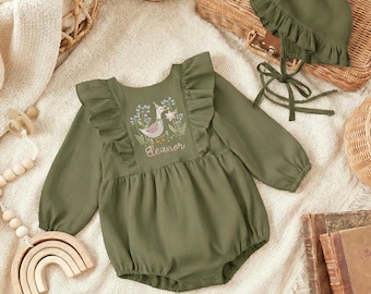 May include: Olive green baby romper and matching bonnet. The romper features long sleeves, ruffles, and an embroidered design with a duck and floral elements. The name "Eleanor" is embroidered below the design. The bonnet has a ruffled brim and tie closure.