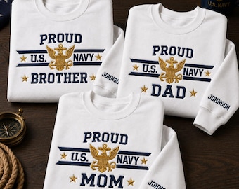 May include: Three white crewneck sweatshirts featuring embroidered U.S. Navy insignia in gold and navy blue. Each shirt displays the text PROUD U.S. NAVY with BROTHER, DAD, or MOM below. The sleeves are personalized with the name JOHNSON in navy blue.