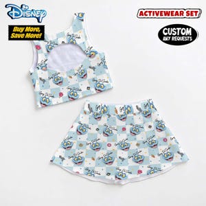 May include: Light blue activewear set featuring a crop top and skirt with a checkered pattern and cartoon character graphics. The set includes the text "Gary Di Sake" and "Disney" branding. The set is designed for active use.